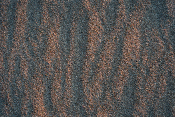 照片背景纹理的沙滩上的沙子照亮了太阳在日落。图片下载