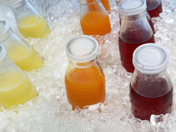 全画幅图片，金属托盘里装满了冰镇的冷果汁饮料，周围是冰块、碎冰和螺旋盖的菠萝汁、橙汁和蔓越莓汁，不含酒精的饮料装在玻璃瓶里，上面有冷凝物，高架视图图片下载
