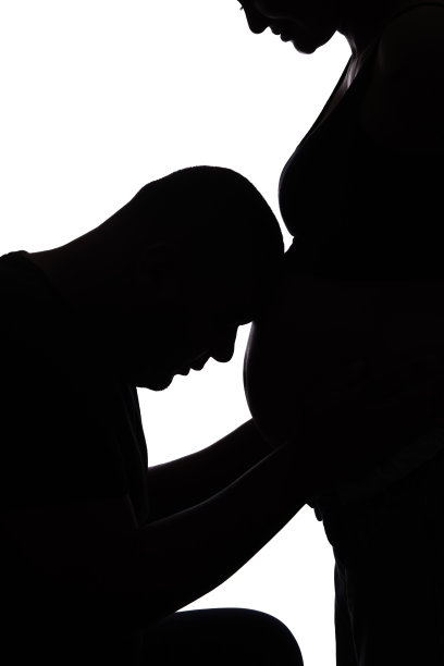 逆光下孕妇的肚子，准爸爸把头靠在肚子上。图片下载