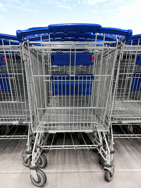 图片中，超市里一排排的购物车在停车场里排成一排，零售购物车区，阳光明媚的蓝色多云的天空为背景，聚焦于前景图片下载