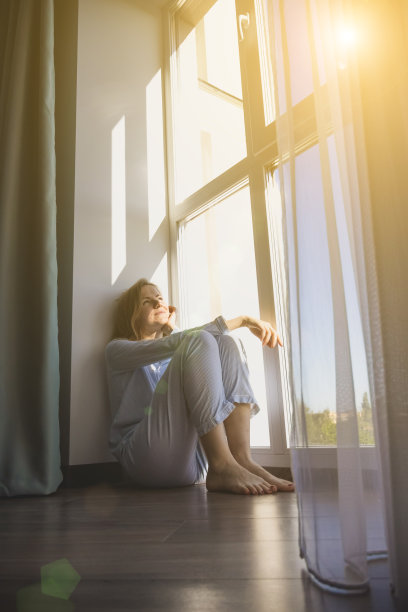 一个女人赤脚坐在地板上的垂直照片。地暖和智能供暖的概念。图片下载
