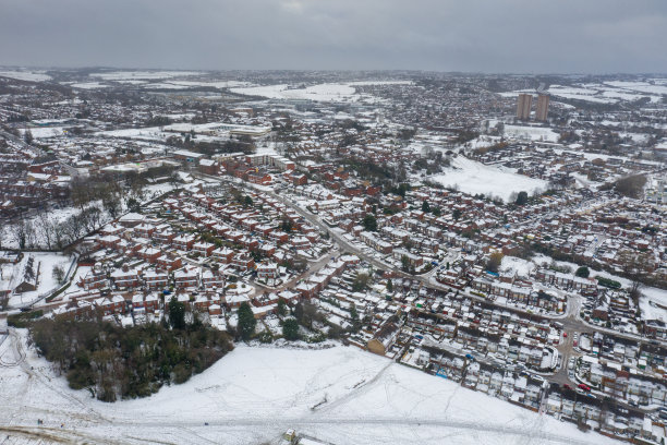 这是英国利兹市下雪天的航拍照片，展示了冬季比斯顿村一排排屋顶被雪覆盖的排屋图片下载