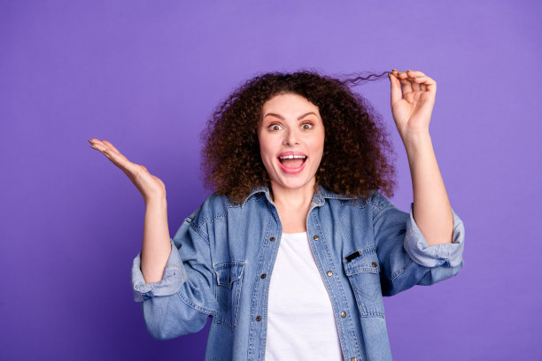 照片凉爽漂亮的女孩手臂持有头发卷发穿牛仔衬衫孤立的紫罗兰色背景图片下载