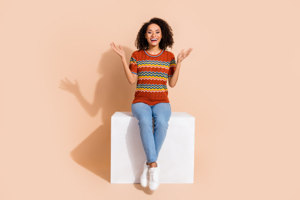 满意的漂亮女孩全身照片穿着装饰t恤牛仔裤坐在站台上拍她的手孤立在柔和的颜色背景图片下载