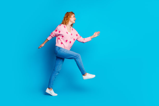 有魅力的年轻女子穿着时髦的粉红色衣服在蓝色背景上跑步的全身照片图片下载