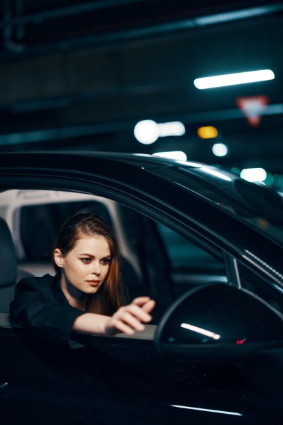 这是一张晚上从侧面拍摄的垂直照片，一个女人坐在车里，看着窗外，把手伸向侧视镜图片下载