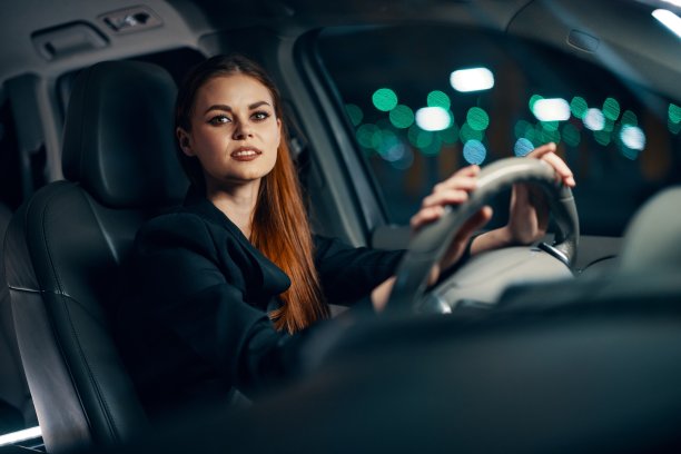 一个可爱、放松的女人坐在汽车方向盘后面的横向照片，在放松的状态下愉快地微笑着。关于安全驾驶主题的照片图片下载
