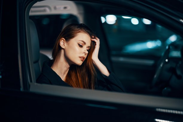 侧面的横向照片，晚上，一个女人坐在一辆黑色的车里，用手捂着脸，脸上带着疲惫的表情，把车停在停车场图片下载