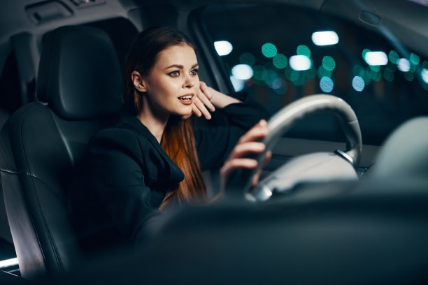一个可爱、放松的女人坐在汽车方向盘后面的横向照片，在放松的状态下愉快地微笑着。关于安全驾驶主题的照片图片下载