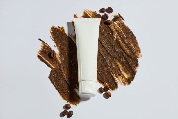 白色的背景上有棕色的奶油条纹，上面有一个没有标签的化妆管，周围装饰着一些咖啡豆。宣传照片，复印空间和高角度拍摄图片下载