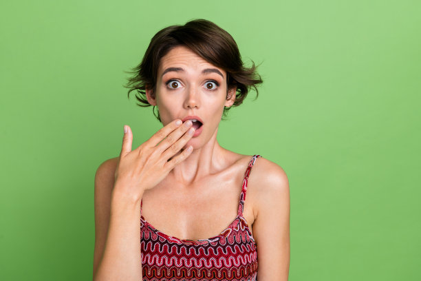 照片中焦虑尴尬的女人穿着时尚的衣服，手捂嘴omg孤立在绿色的背景图片下载