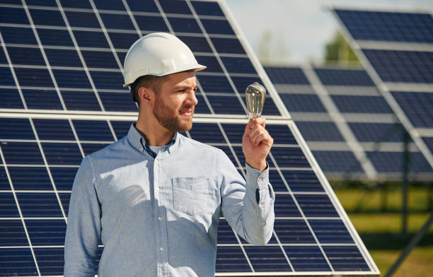 手里拿着灯泡。白天在户外使用光伏太阳能电池板的工程师图片下载