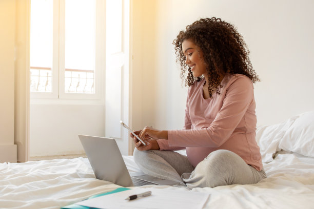 家庭办公室。黑人孕妇在家用智能手机和笔记本电脑工作图片下载