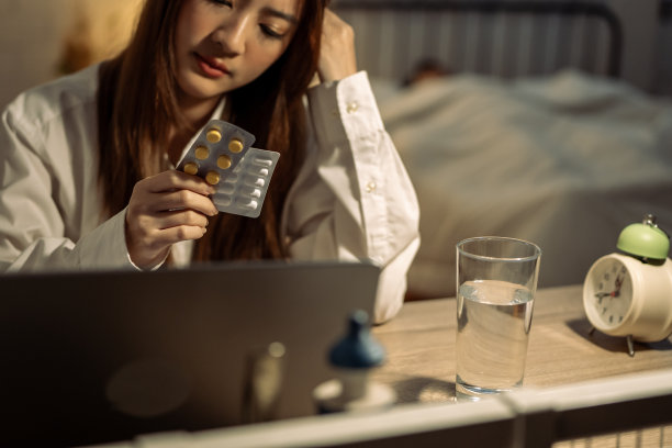 亚洲不开心的生病女孩穿着睡衣在床上睡觉前吃药。迷人美丽的年轻女子在家里咳嗽发烧后，在漆黑的卧室里服用了许多药物。Healthcare-medical概念图片下载