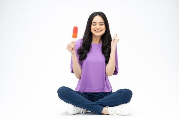 照片中，开朗可爱的女人穿着时髦的衣服，坐在地板上吃冰淇淋，空白的空间被隔离在白色的背景上图片下载