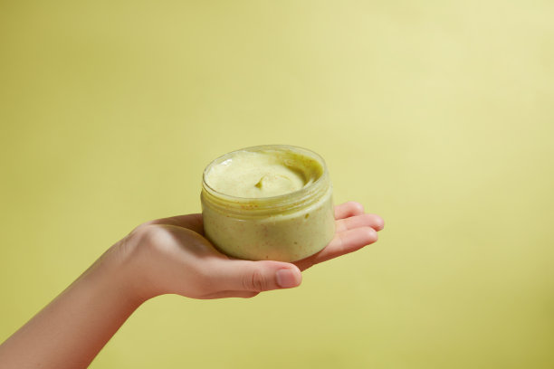 一个黄色的去角质壶放在一个美丽的手在中心，在淡黄色的背景。正面照片，有许多空白的空间，用于设计和添加文字图片下载