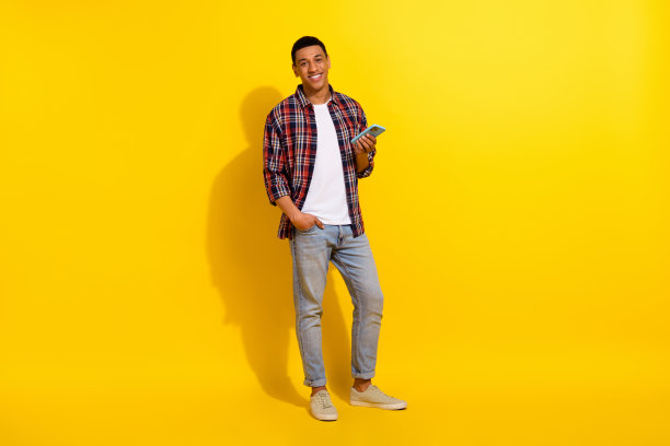 智能男子穿格子衬衫牛仔裤的全长照片手臂在口袋里拿智能手机孤立在生动的色彩背景图片下载