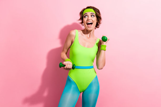 照片中的美女哑铃练习穿着时髦的绿色运动连衣裤孤立在粉红色的背景图片下载
