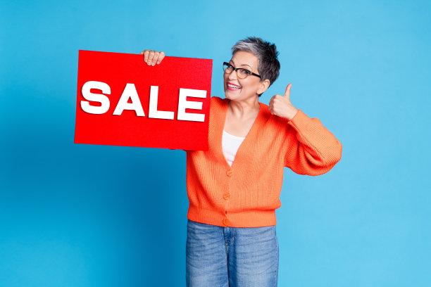 可爱的高级女士的照片肖像手持销售板横幅拇指向上穿着时尚的橙色服装孤立在蓝色背景图片下载