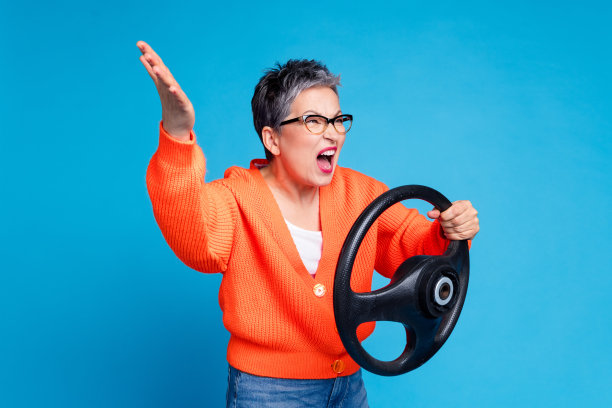 可爱的高级女士的照片肖像拿着方向盘烦恼穿着时尚的橙色服装孤立在蓝色背景图片下载