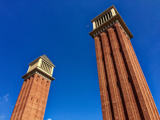 这张照片显示了在晴朗的蓝天下，两座带有白色建筑细节的高大红砖塔。图片下载