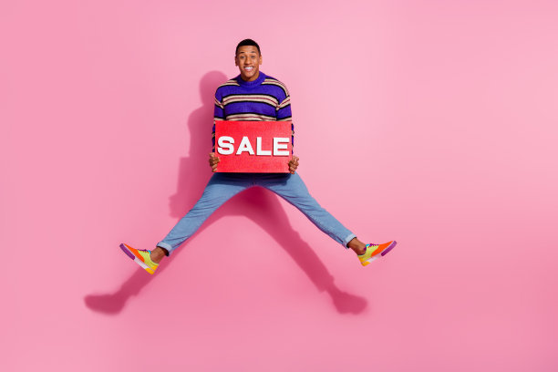 正面好心情的男人穿条纹毛衣跳高拿出售板空空间孤立的粉红色背景的全身照片图片下载