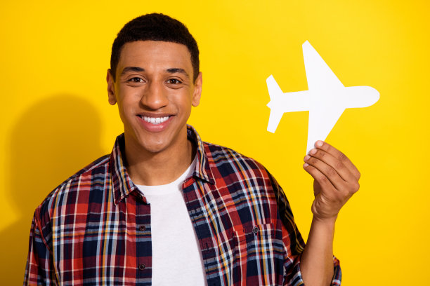 照片中，一个留着时髦发型、穿着格子衬衫、笑容满面的男子手持白色的纸飞机，孤立在黄色的背景上图片下载
