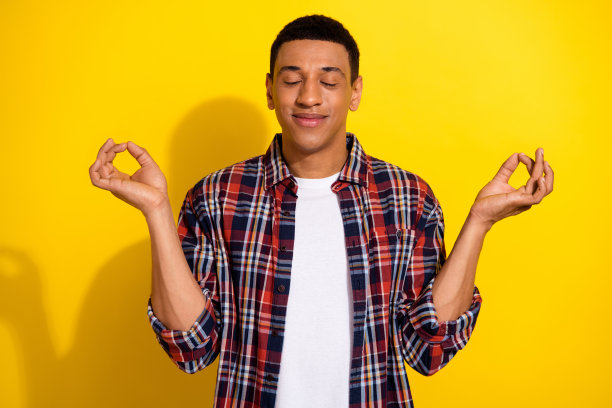 照片中，和蔼开朗的男人闭着眼睛，穿着时髦的衣服，在黄色背景上孤立的莲花标志图片下载