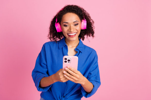 照片中可爱可爱的女人穿着时髦的衣服，听着音乐，蓝牙耳机，在粉红色的背景下聊天图片下载