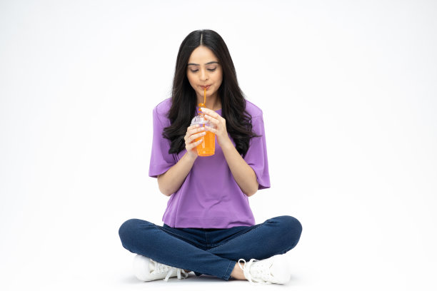 开朗可爱的女人穿着时髦的衣服，坐在地板上喝果汁，空白的空间孤立在白色背景的照片图片下载