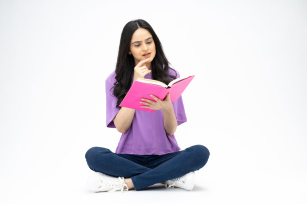 开朗可爱的女人穿着时髦的衣服，坐在地板上看书，空白的空间孤立在白色背景的照片图片下载