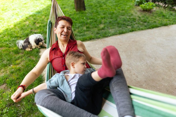 孙子和奶奶躺在院子里的躺椅上。祖母是有血有肉的种族，x一代。男孩皮肤和头发都很白。他们通过玩耍、拥抱和微笑享受在一起的时光。焊接时间。复制空间，库存照片图片下载