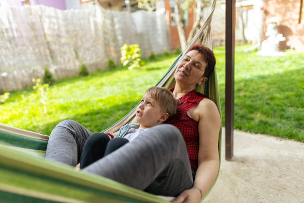 孙子和奶奶躺在院子里的躺椅上。祖母是有血有肉的种族，x一代。男孩皮肤和头发都很白。他们通过玩耍、拥抱和微笑享受在一起的时光。焊接时间。复制空间，库存照片图片下载