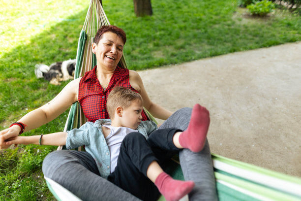 春天的一天，孙子和奶奶躺在院子里的躺椅上。祖母是有血有肉的种族，x一代。男孩皮肤和头发都很白。他们通过玩耍、拥抱和微笑享受在一起的时光。焊接时间。复制空间，库存照片图片下载