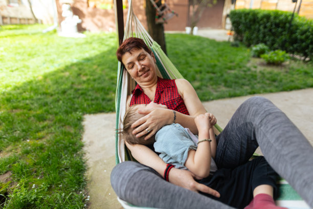 孙子和奶奶躺在院子里的躺椅上。祖母是有血有肉的种族，x一代。男孩皮肤和头发都很白。他们通过玩耍、拥抱和微笑享受在一起的时光。焊接时间。复制空间，库存照片图片下载