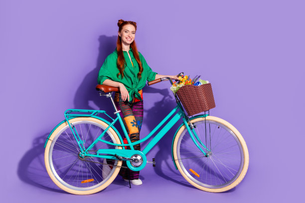 全尺寸照片可爱的积极的女人穿着绿色衬衫复古裤子拿着自行车与花朵孤立的紫色背景图片下载