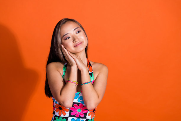 梦幻女人的照片，直发，穿着印花连衣裙，看着销售空白的空间，手臂在脸颊上孤立的橙色背景图片下载