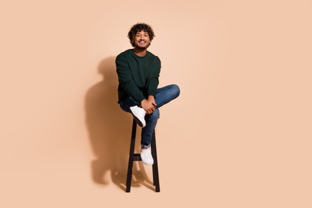 全身照片开朗迷人的家伙穿着运动衫坐在酒吧椅子空的空间孤立米色背景图片下载