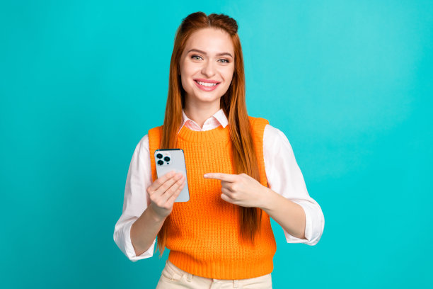 照片中可爱的小女孩穿着时尚的橙色衣服，在青色的背景下为现代小工具苹果手机做广告图片下载