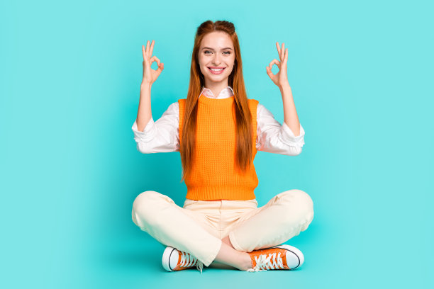 照片中可爱可爱的女孩穿着橙色时尚的衣服，坐在地板上，在青色的背景上显示出好的标志图片下载