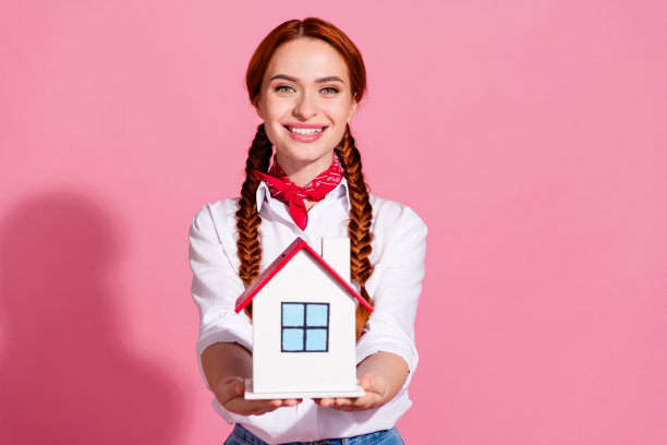 照片中可爱可爱的女孩穿着时髦的衣服，双手抱着房子，舒适的公寓，孤立在粉红色的背景上图片下载