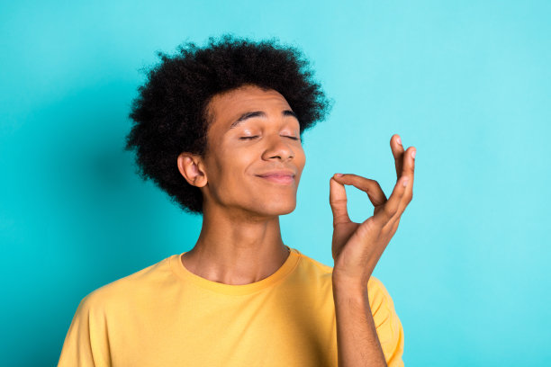 照片中快乐的家伙，留着非洲式发型，穿着黄色t恤，闭着眼睛，梦想着在绿松石色的背景上孤立的美味蛋糕图片下载