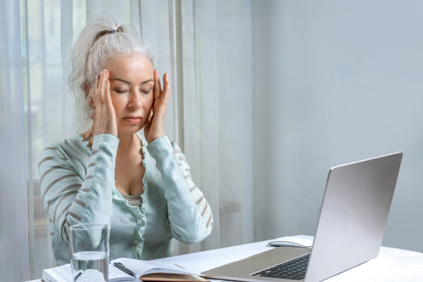 一位老妇人因长时间在电脑前工作而感到疲劳和头痛。图片下载