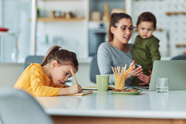 一个有创意的小女孩在她的笔记本上画画，而她的妈妈在家里工作图片下载