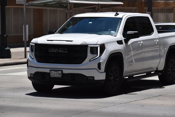 一辆白色的GMC Sierra 1500 HD的肖像，带有白天行驶的大灯，在市中心巡航图片下载