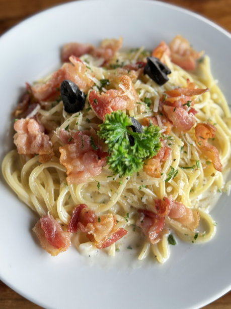意大利面条的特写图片，以培根、帕尔马干酪、切碎的大蒜、鸡蛋、半黑橄榄、欧芹叶装饰在白色盘子上，木制餐厅桌子背景，高架视图图片下载