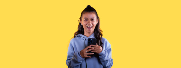 生活方式:黄色背景的年轻拉丁人在智能手机上聊天，脸上带着高兴或惊讶的表情图片下载