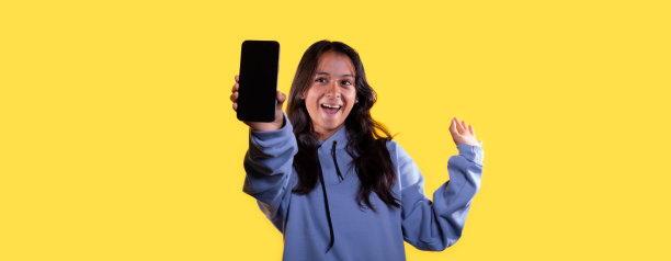 生活方式:黄色背景下的年轻拉丁人，情绪激动地展示着她的智能手机屏幕图片下载