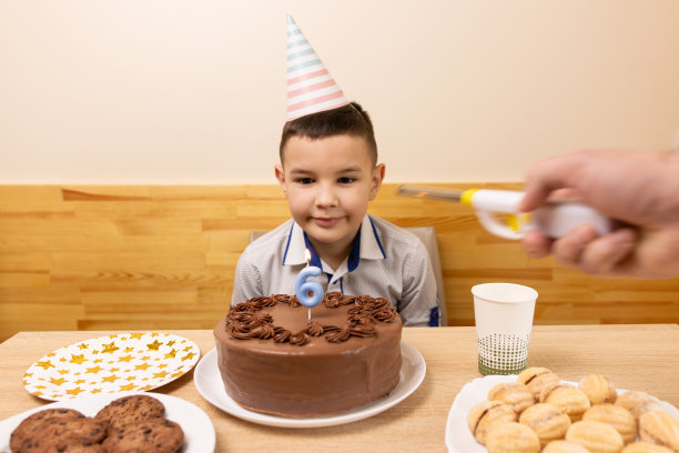 一个男孩坐在桌子前，桌上放着一个节日蛋糕，蛋糕上点燃了一支数字6的蜡烛。生日庆祝的概念。图片下载