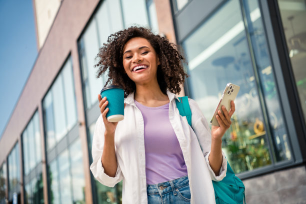 可爱兴奋的女士穿着白衬衫背包喝茶发短信在城市街道外的现代设备的照片图片下载